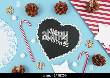 Weihnachten flach mit herzförmigen Schiefertafel mit Text "Frohe Weihnachten!" auf hellblauem Hintergrund mit saisonale Dekoration wie Candy Cane Stockfoto