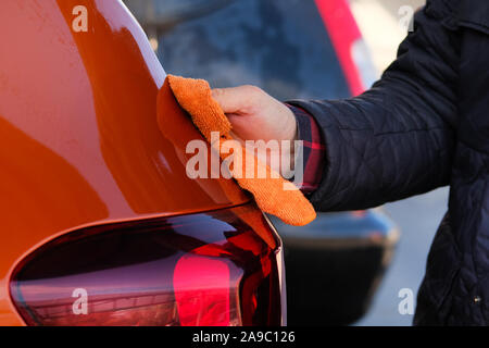 Mann nach dem Waschen wischt seine orange Auto mit einem Lappen am Auto waschen. Männliche Hand und Karosserie. Stockfoto