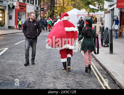 Der Weihnachtsmann und eine weibliche Elfe weg gehen Hand in Hand, Blick von Passanten auf die London Street Stockfoto