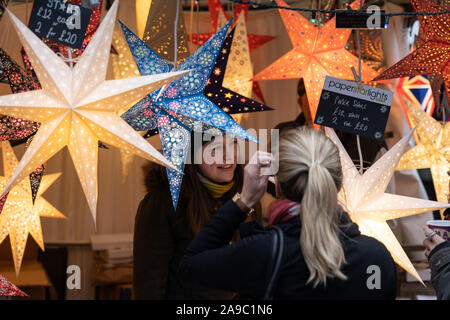 Auf dem Weihnachtsmarkt in Harrogate, North Yorkshire, England, verkauft eine Frau Diwali Star Lights und Laternen. Stockfoto