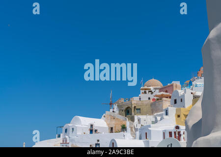 Oia, Santorini, Griechenland - 7. August 2019; Häuser und Gebäude in Weiß mit Farbakzenten im traditionellen griechischen Stil der Insel unter blauem Himmel. Stockfoto