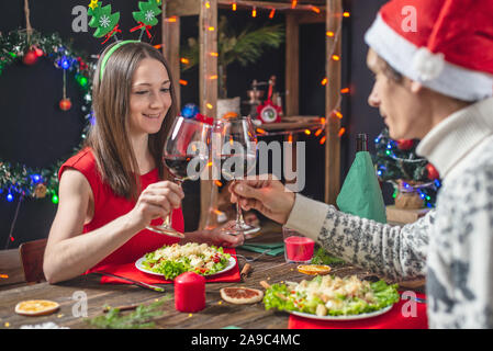 Junge schöne Paar Liebhaber verbringen Sie einen festlichen Abend Wein trinken aus Gläsern und klirren Gläser in der Weihnachtsschmuck auf's Neue Jahr ev Stockfoto