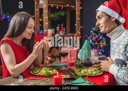 Ein Mann hält ein Geschenk für seine Geliebte. Eine junge schöne Paar Liebhaber verbringen Sie ein festliches Abendessen im Weihnachtsschmuck Stockfoto