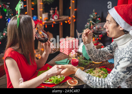 Junge schöne Paar Mann und Frau verbringen einen festlichen Abend speisen und trinken Wein aus Gläsern in die Weihnachtsdekorationen an Silvester Stockfoto