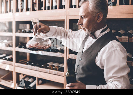 Sommelier Konzept. Älterer Mann stehend an Wein Dekanter Kontrolle Sediment konzentriert Seitenansicht suchen Stockfoto