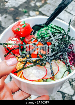 Poke Schüssel mit Thunfisch in das verfügbare Papier container. Frau hand mit traditionellen Hawaiianischen fast food auf einer Straße der Stadt. Mobile Fotografie Stockfoto