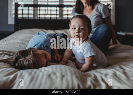 Baby Mädchen sitzen auf dem Bett mit Mama und 5 Jahre alten Bruder in der Nähe der Fenster Stockfoto