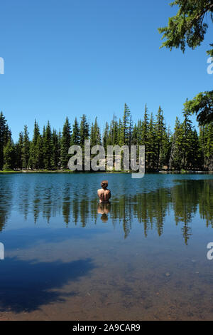 Mann in einem See mit Reflexionen von Körper, Bäume, und Sky Stockfoto