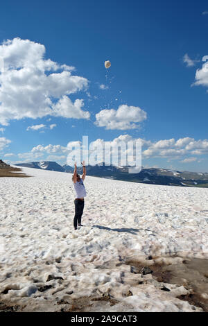 Mann im T-Shirt werfen Schneeball in der Luft im Schneefeld in den Bergen Stockfoto