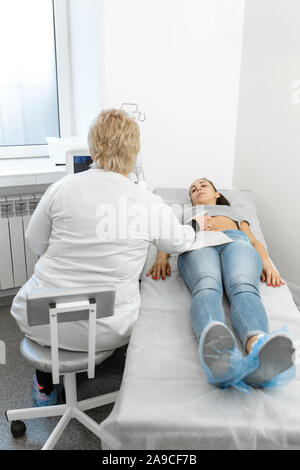 Der Arzt führt eine Ultraschall- Diagnostik des Abdomens und der inneren Organe des Patienten. Ein Mädchen liegt auf einer Couch in ein Ultraschall Diagnose Zimmer Stockfoto