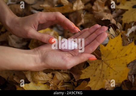 Weibliche hand mit orange Maniküre Holding rosa Quarz yoni Ei für vumfit, imbuilding oder Meditation auf gelbem Hintergrund Laub im Herbst Stockfoto