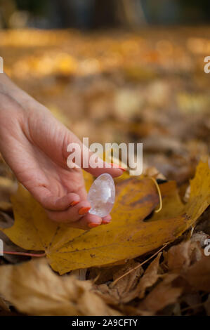 Weibliche hand mit orange Maniküre Holding transparent violett Amethyst yoni Ei für vumfit, imbuilding oder Meditation auf gelbem Laub Hintergrund Stockfoto