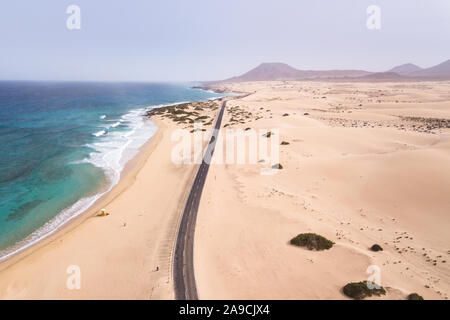 Strand Luftaufnahme mit einer Straße entlang Ozean Küste und Sanddünen auf Fuerteventura, Kanarische Inseln gesehen von Drohne, malerischen Küste Landschaft, Sommer Stockfoto
