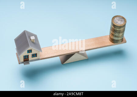 Eine Ansicht von Miniatur Haus und Münze Stapeln auf Holz- Wippe vor blauem Hintergrund Stockfoto
