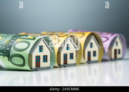 Reihe der Miniatur Häuser innerhalb der Euro-banknoten auf weißem Schreibtisch gegen grauer Hintergrund Stockfoto