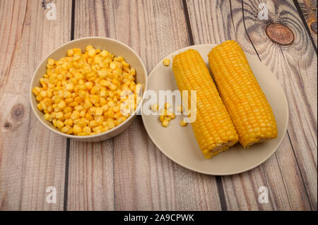 Zwei Ohren von gekochten Mais in eine Platte und ein Korn von Korn auf dem Tisch. Gesunde Ernährung. Fitness Ernährung. Für einen süßen Leckereien Stockfoto