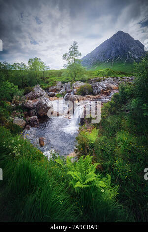 Kleiner Wasserfall zwischen dem Gras und ein Berg im Glen Etive Tal, in den Highlands von Schottland. Etive River. Bewölkten Tag. Stockfoto