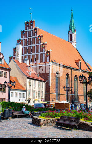 Riga mittelalterliche Altstadt, St. John's Church, schöner Garten mit Bänken und Touristen, vertikal Stockfoto