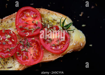 Ein Stück italienisches Weißbrot mit grünen Oliven öl- und Tomatenscheiben mit Oregano gewürzt gegen einen dunklen Hintergrund Stockfoto