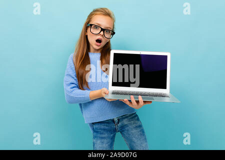 Überrascht, schockiert Schulmädchen auf blauem Hintergrund hält den Laptop mit dem Bildschirm nach vorn Stockfoto