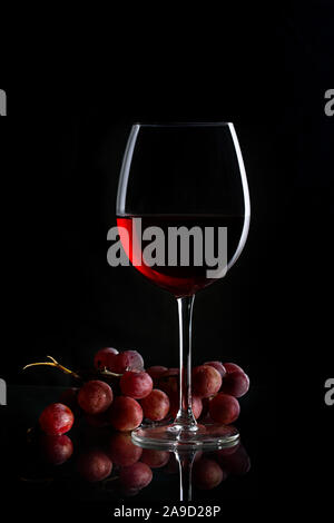 Glas Rotwein und Trauben auf dem dunklen Hintergrund Stockfoto