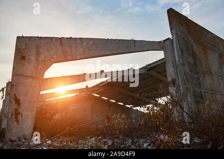 Konkrete Balken und Wände der zerstörten alten Lagerhaus in den Strahlen der aufgehenden Sonne. Stockfoto
