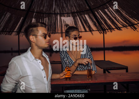 Sommer. Zwei jungen Freunden Bier trinken, während Sie in einer guten Stimmung in der Beach Bar. Lifestyle, Freundschaften, Ferienhäuser Konzept Stockfoto
