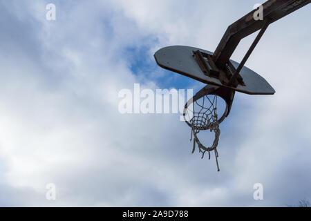 Der zerfetzten Net eines gut Basketball Ziel gegen einen bewölkten Himmel mit einem Patch von Blau. Stockfoto