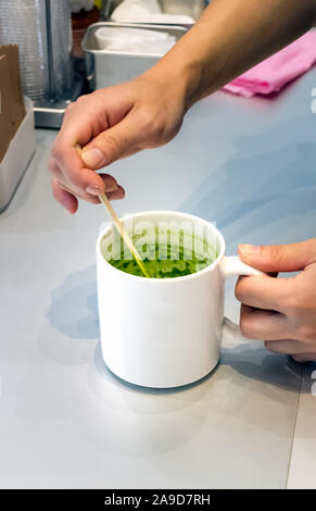 Weibliche barista Hand rühren Matcha grüner Tee auf einer Tasse. Stockfoto