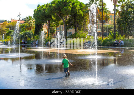 Ein Junge mit einem Hut spielt und spritzt in der Promenade du Paillon Park in der touristischen Altstadt von Nizza, Frankreich an der Französischen Riviera. Stockfoto