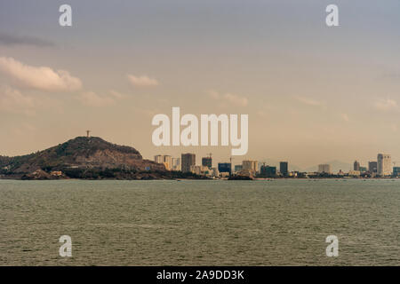 Vung Tau, Vietnam - 12. März 2019: Skyline der Stadt mit hohen Gebäuden neben Wald bedeckten Hügel mit auf riesigen Jesus Christus Statue Stockfoto