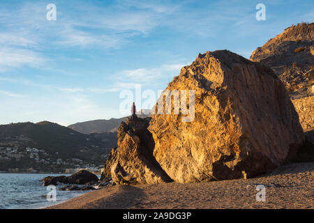 Ein Mann steht auf einem riesigen Felsen kletterte er hat, mit Blick auf das Meer am La Herradura Strand in Spanien. Stockfoto