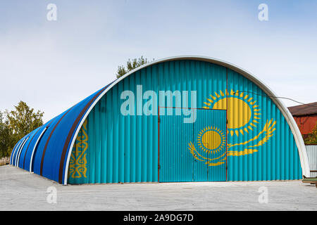 Nahaufnahme der nationalen Flagge Kasachstan auf dem Metall Wand einer großen Lagerhalle gemalt das geschlossene Territorium gegen den blauen Himmel. Das Konzept der Stora Stockfoto