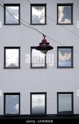 Eine hängelampe vor der Fassade eines Wohnhauses mit Windows, in der die Wolken reflektiert werden. Stockfoto