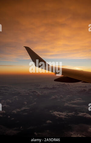 Flugzeugflügel bei Sonnenaufgang über den Wolken Stockfoto