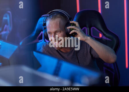Happy bärtige junge Gamer in Kopfhörer am Computer Monitor schauen und Lachen im dunklen Zimmer sitzen Stockfoto