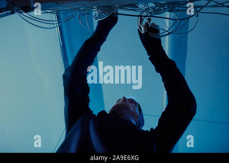 Low Angle View junger Mann in dunkler Kleidung, setzen Sie die Drähte, um in dunklen Zimmer Stockfoto