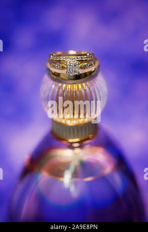Trauringe auf der Deckel einer Parfumflasche gegen einen violetten Hintergrund Stockfoto