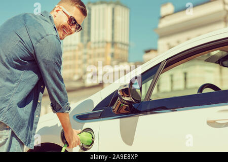 Positiv erfreut, blonder Mann seinen Elektro Auto aufladen Stockfoto