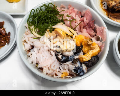 Die koreanische Küche - Blick von oben auf die verschiedenen Meeresfrüchten und gehackte rohe Fische oben Kimchi mit Sojasauce in Weiß Schüssel auf dem Tisch in einem lokalen Restaurant in Seoul ci Stockfoto
