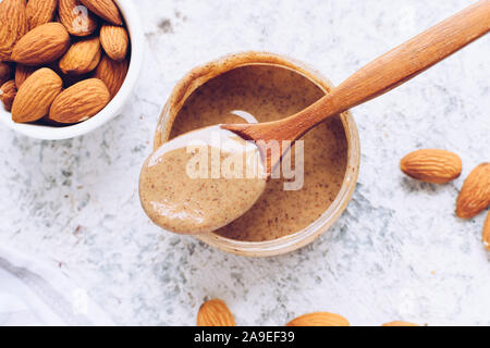 Mandel Mutter Butter in Glas. Hausgemachte organischen Mandel Muttern einfügen auf grauem Hintergrund. Gesunde natürliche Lebensmittel Konzept. Ansicht von oben. Stockfoto
