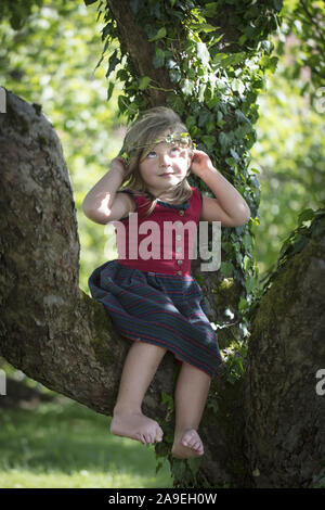 Kind mit Efeu Rebe auf Kopf, sitzen in einem Apple tree Stockfoto