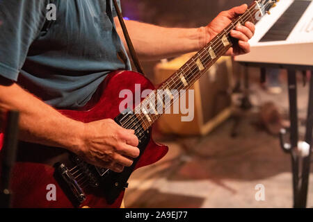 Nahaufnahme und selektiven Fokus auf Red elektrische Gitarre des Menschen, wie er spielt, mit einem verschwommenen Studio im Hintergrund Stockfoto