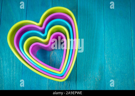 Farbige herzförmige Ausstechform Figuren sitzen auf Blau Holz- Hintergrund und und Gesehen von oben Stockfoto
