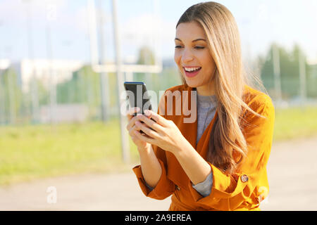 Gerne schöne Frau gehen und das Schreiben oder Lesen von SMS-Nachrichten online auf einem Smartphone. Stockfoto