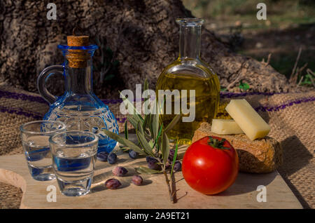Kretische Küche mit nativem Olivenöl, Oliven, kretische Gerstenzwieback, Käse und Karaffe kretische Raki. Stockfoto