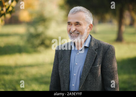 Portrait von Happy älterer Mann im Park. Grauhaarige bärtigen Mann in Grau Jacke Stockfoto