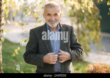 Portrait von Happy älterer Mann im Park. Grauhaarige bärtigen Mann in Grau Jacke Stockfoto