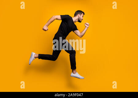 Volle Länge Profil Foto von Stattlichen tausendjährigen Kerl springen hoch hetzen, niedrige Preise Rabatt shopping tragen schwarze T-Shirt Hose gelb isoliert Stockfoto