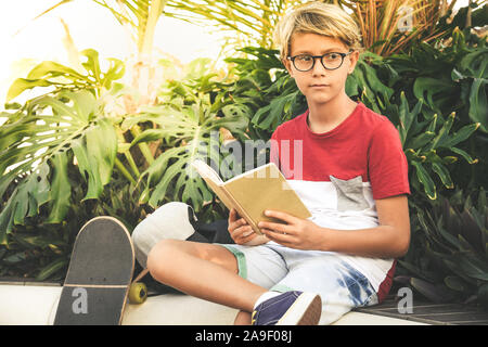 Jugendlich liest ein Buch im Freien. Junge Junge, sitzen in einem exotischen Garten, Hausaufgaben glücklich und sorgenfrei. Porträt einer wunderschönen Studenten ein Studium an der Stockfoto